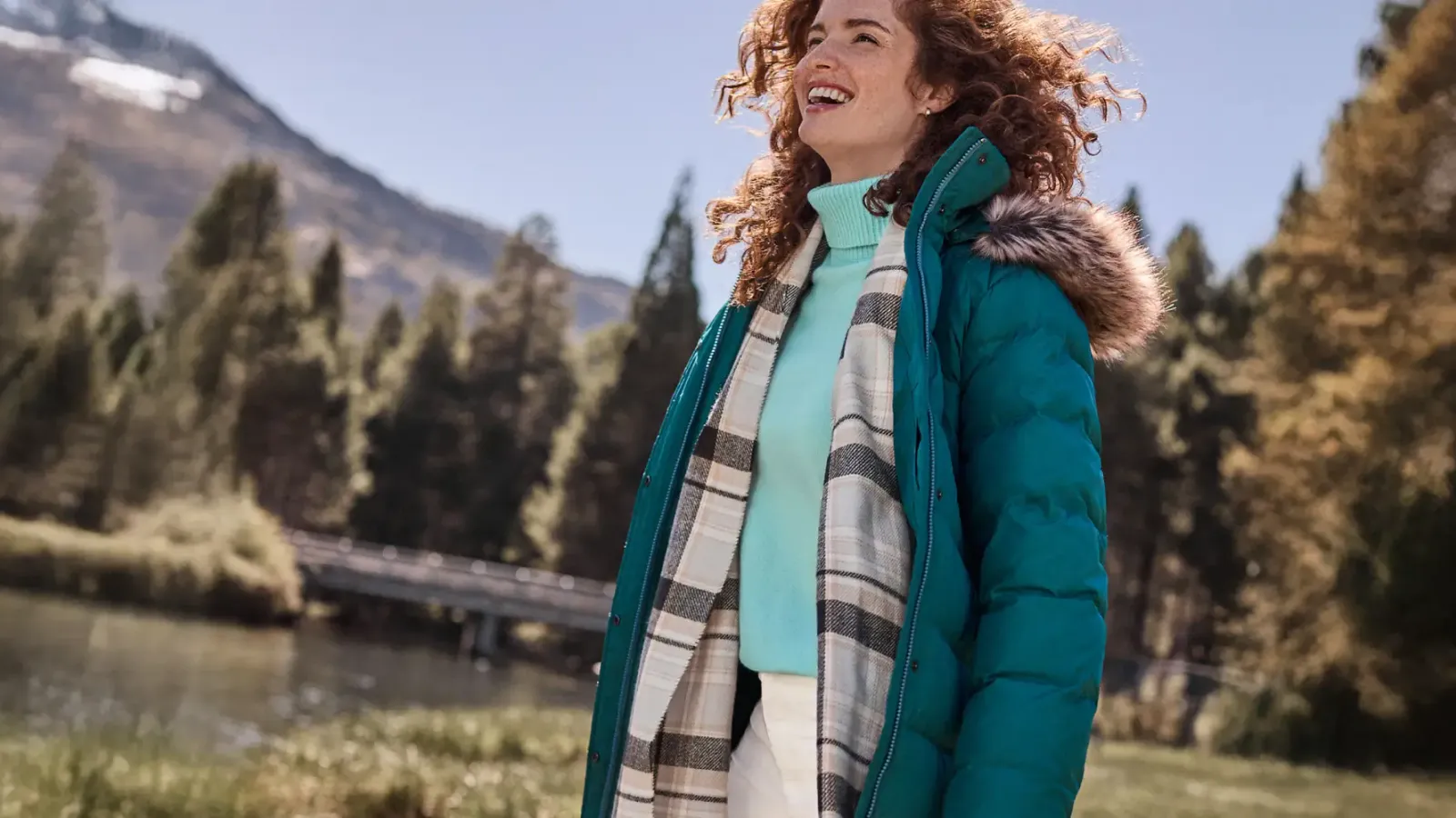 Woman wearing a teal puffer jacket and white and black scarf over a turquoise turtleneck.