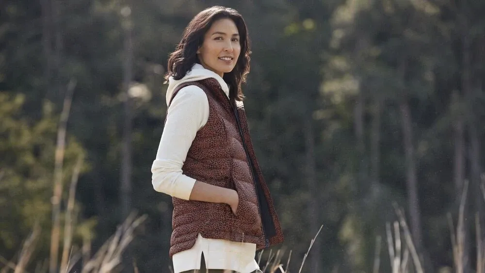 Woman wearing a white hooded sweatshirt and brown puffer vest.