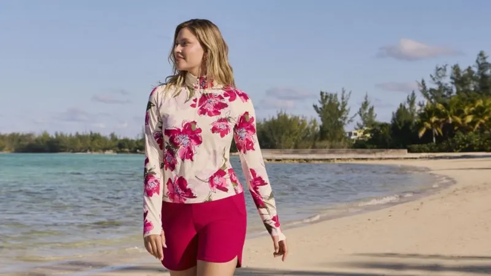 Woman wearing a white and pink floral rashguard and magenta board shorts.