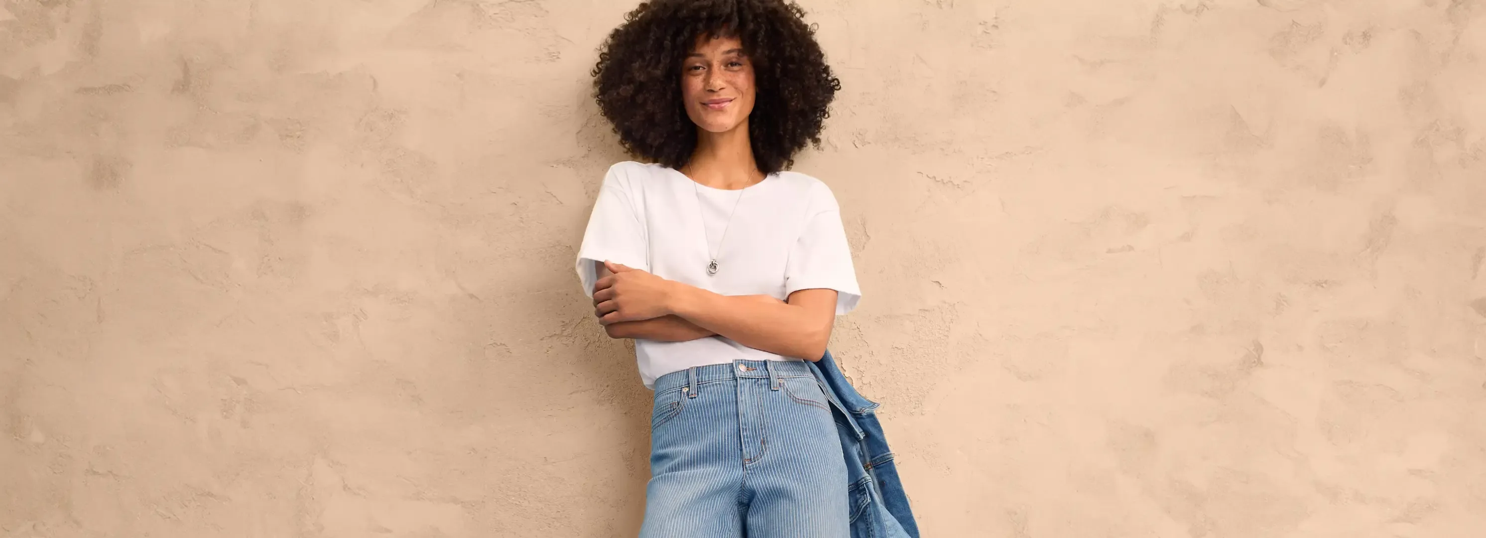 Woman wearing a white shirt and blue jeans holding a jacket.