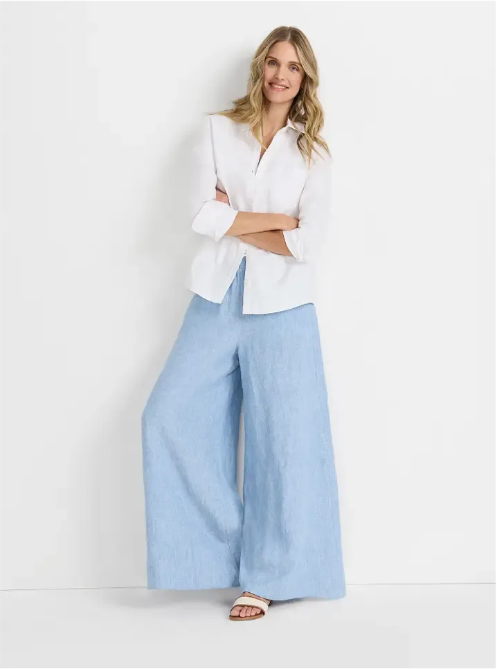 Woman wearing a white button-up shirt and light blue wide-leg pants.