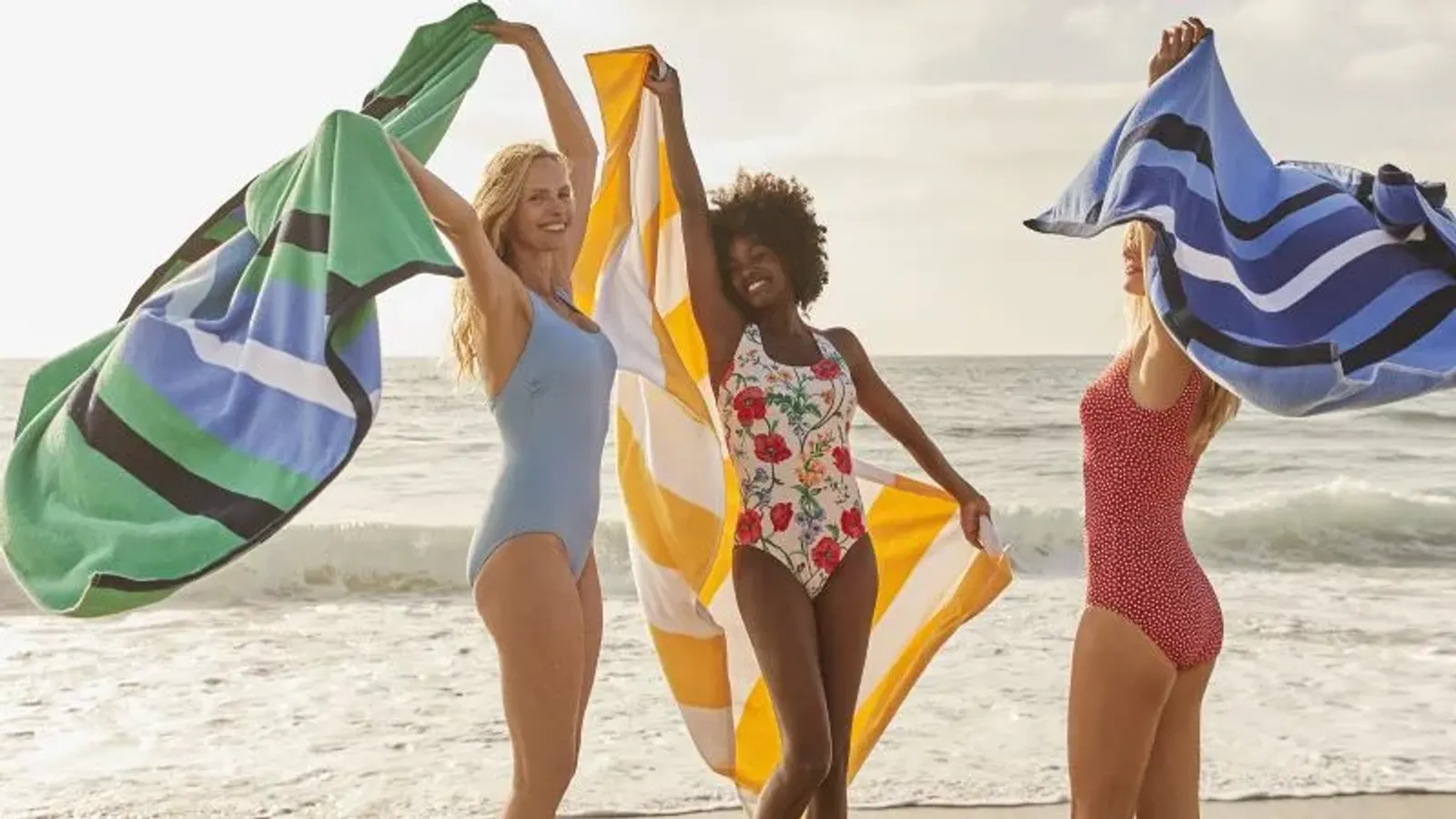 Three women wearing one piece swimsuits and waving beach towels.