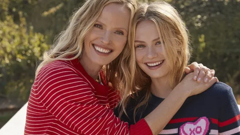 A mother and daughter wear Valentine's sweaters in a warm embrace.