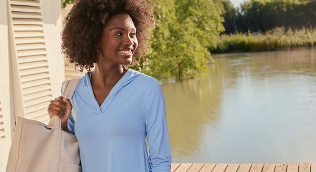 A woman wearing a light blue cover-up holding a canvas tote.