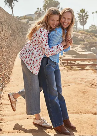 A woman hugging another woman's back on a sandy beach.