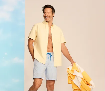 A man wearing an ubuttoned top and swim trunks.