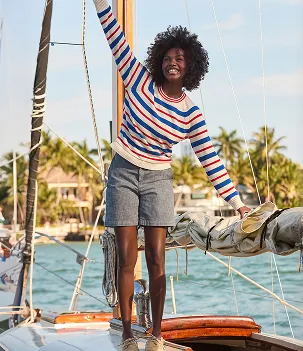 A woman wearing a white, blue, and orange striped shirt with a gray pair of shorts.