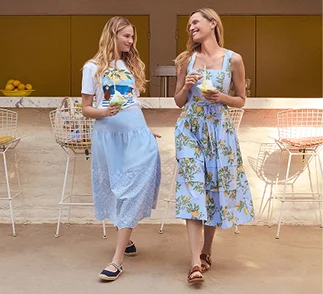 A woman wearing a t-shirt and skirt and a woman wearing a patterned dress at an outdoor bar.