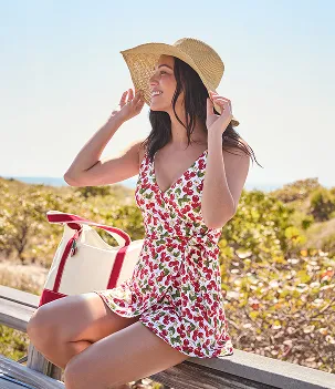 A woman wearing a sun hat and a swim dress with a repeating cherry pattern on it.