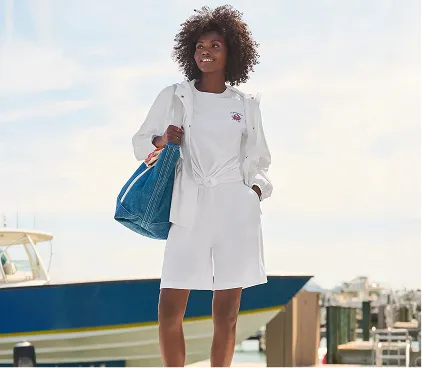 A woman wearing a white top with white shorts holding a denim tote.