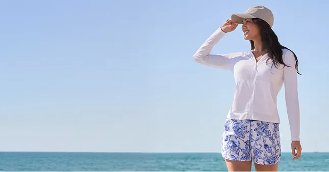 A woman wearing a white top, a gray hat and white and blue floral pattern shorts.