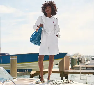 A woman wearing a white top and shorts with a denim tote.