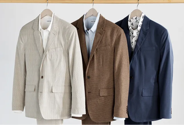 Three suits on a rack in cream, brown, and navy colors.