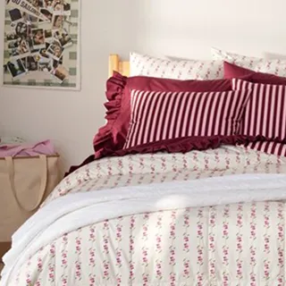 A dorm room bed with a cream colored comforter and red pillows.