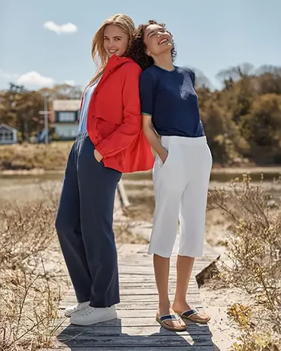 Two women lean back-to-back against each other in a field.