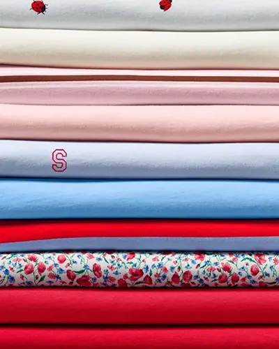 A folded stack of supima tees in different colors and patterns.