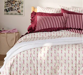 A bed with a cream colored comforter and red pillows.