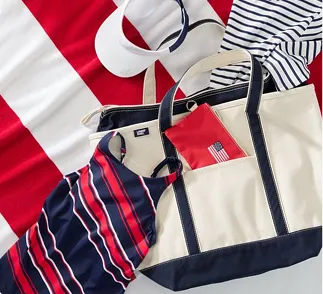 A navy and red pattern swim suit laid ontop of a tote and beach towel.