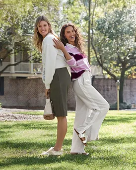 Two women knit tops stand back-to-back to each other.
