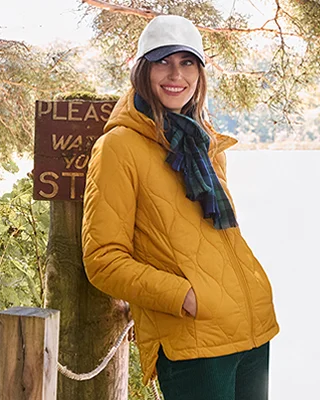 A woamn wearing a yellow jacket and a baseball cap.