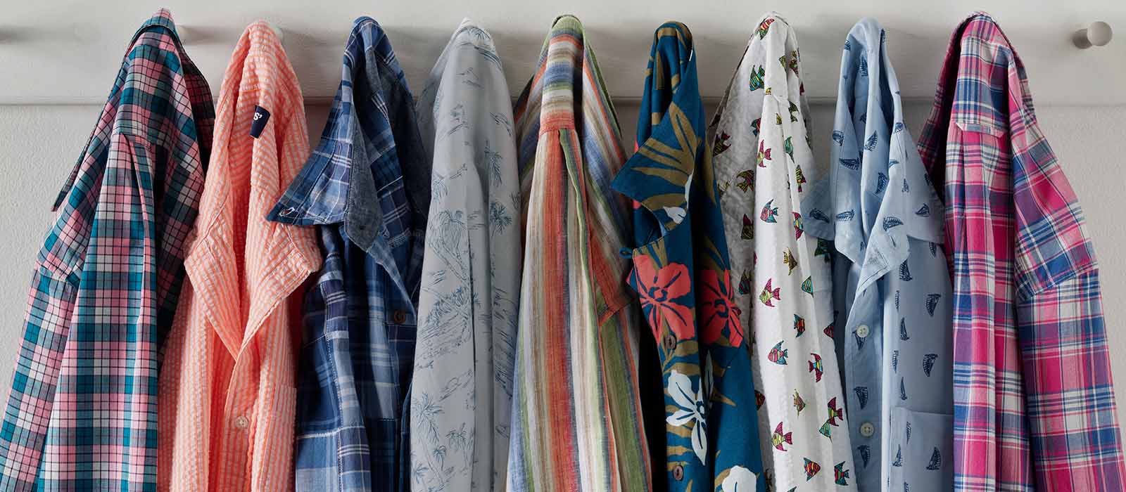 Several shirts of different summer colors and patterns hanging from hooks.