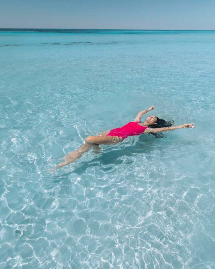 A woman in a red swimsuit floating in clear beach water.