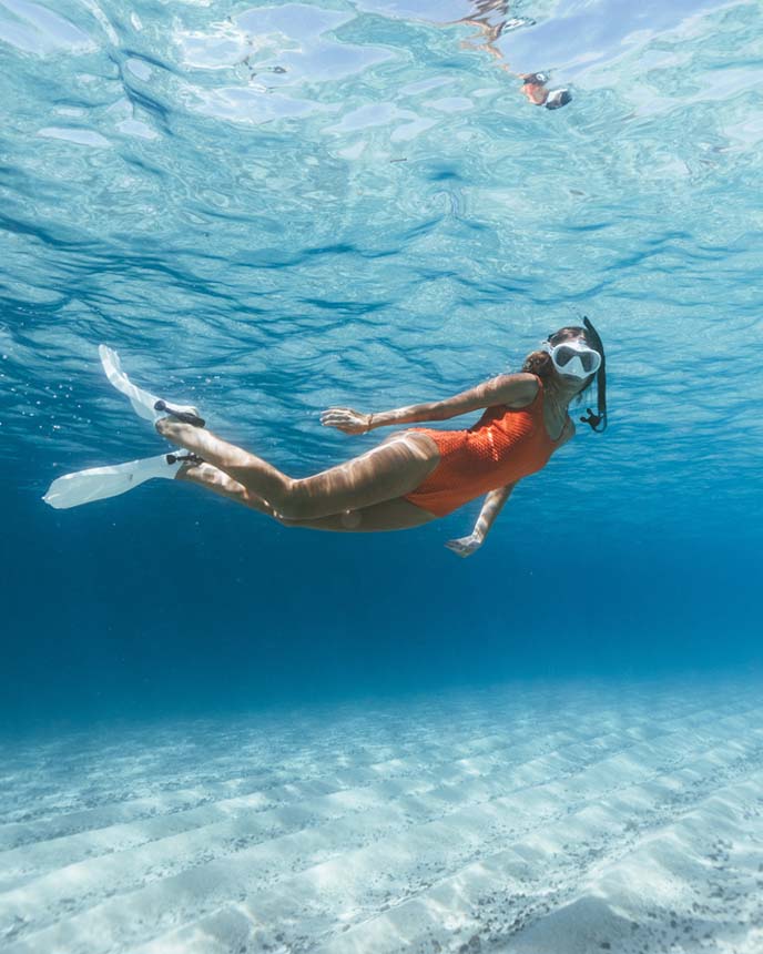 A woman in an orange swimsuit snorkling underwater.