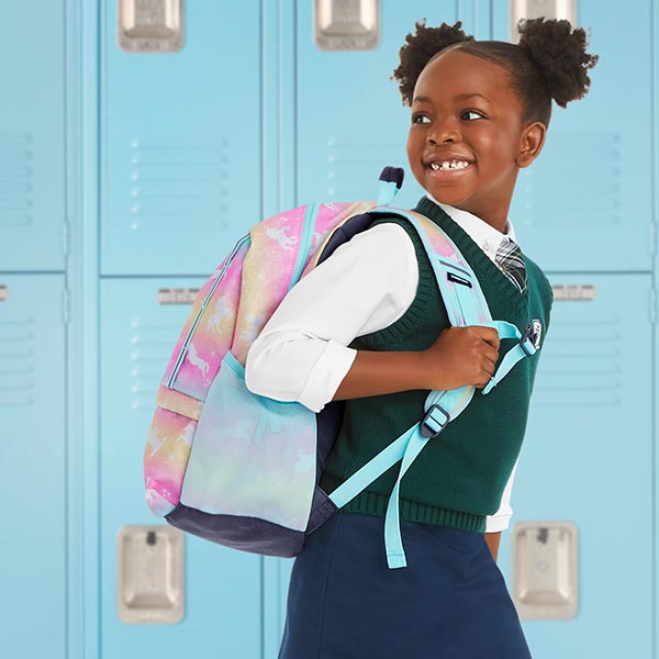 A girl smiling with her backpack on infront of blue school lockers.