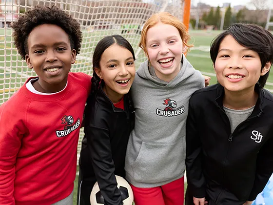 Four students wearing school athleticwear on a soccer field.