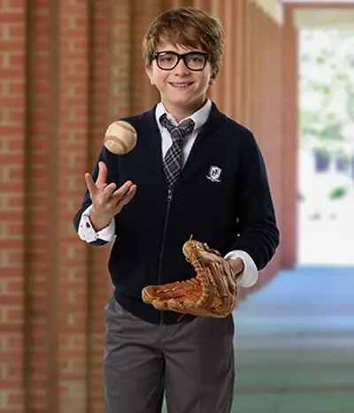A student wearing a navy cardigan tossing a baseball into the air.