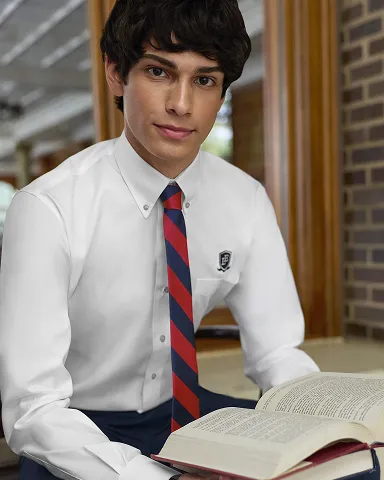 Student wearing a white dress shirt and a red striped tie reads a textbook.